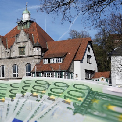 Vor dem Bergisch Gladbacher Rathaus sind aufgefächerte Geldscheine zu sehen.