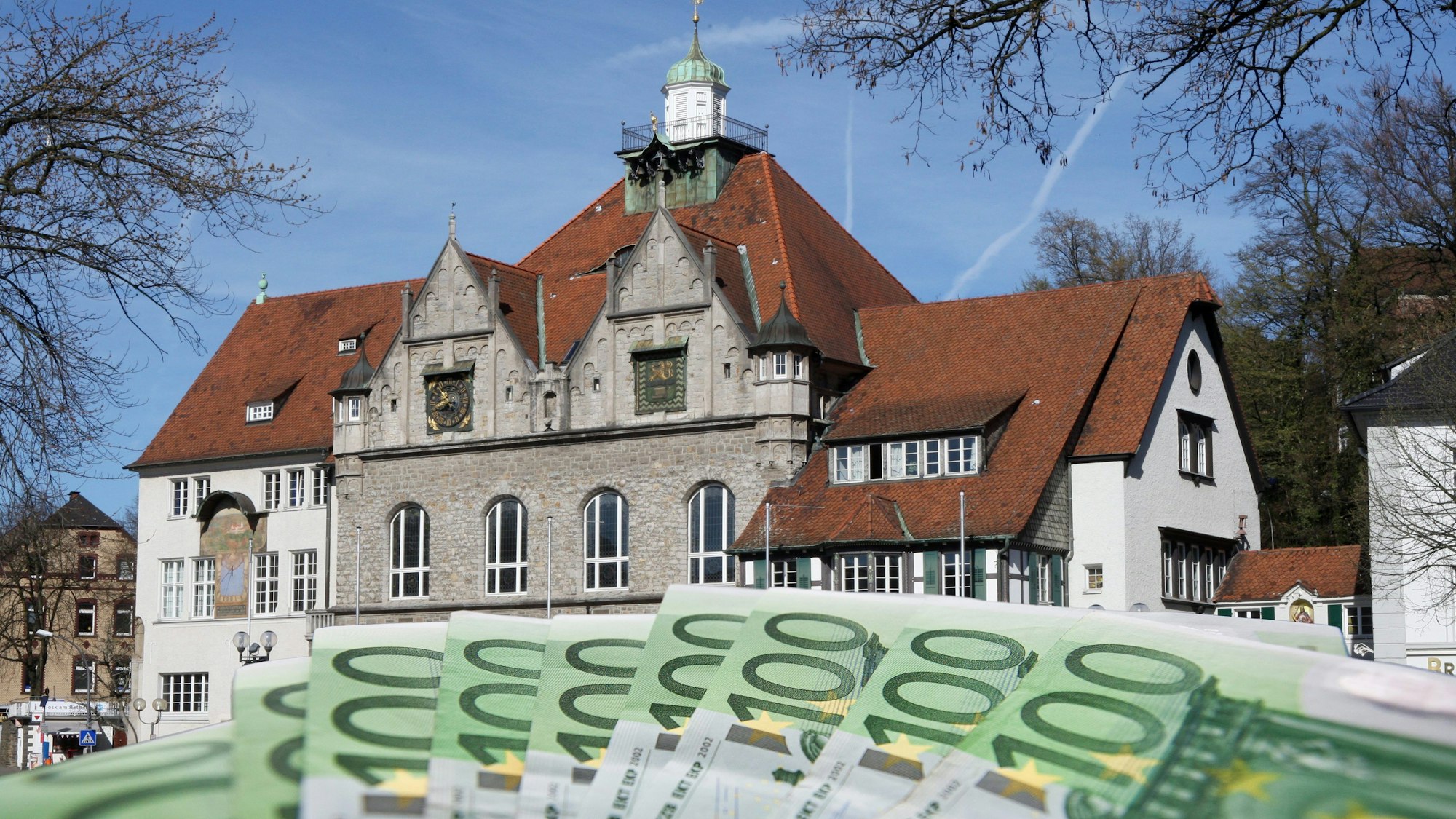 Das historische Rathaus von Bergisch Gladbach, davor aufgefächert grüne 100-Euro-Scheine.