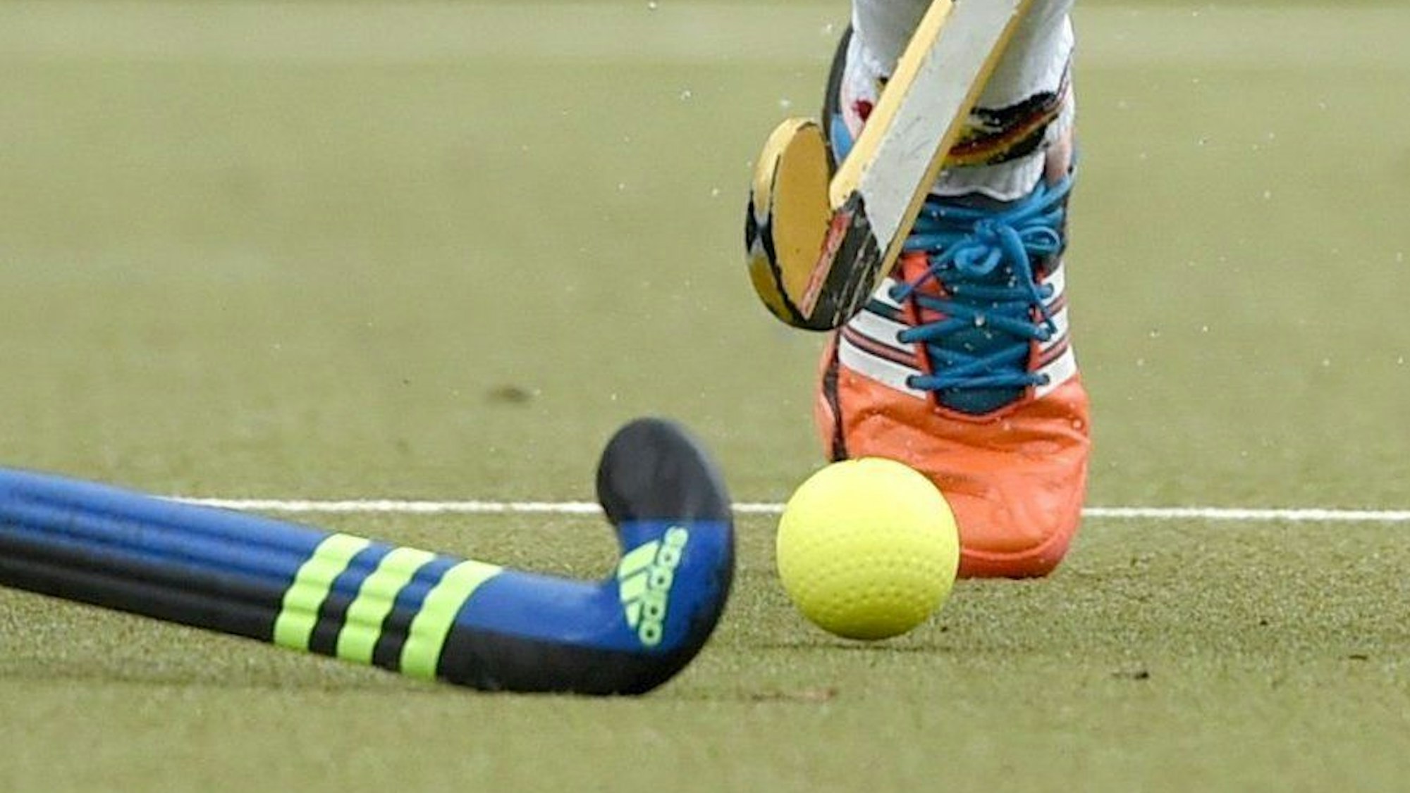 Zwei Feldhockeyschläger zielen in Richtung Ball.