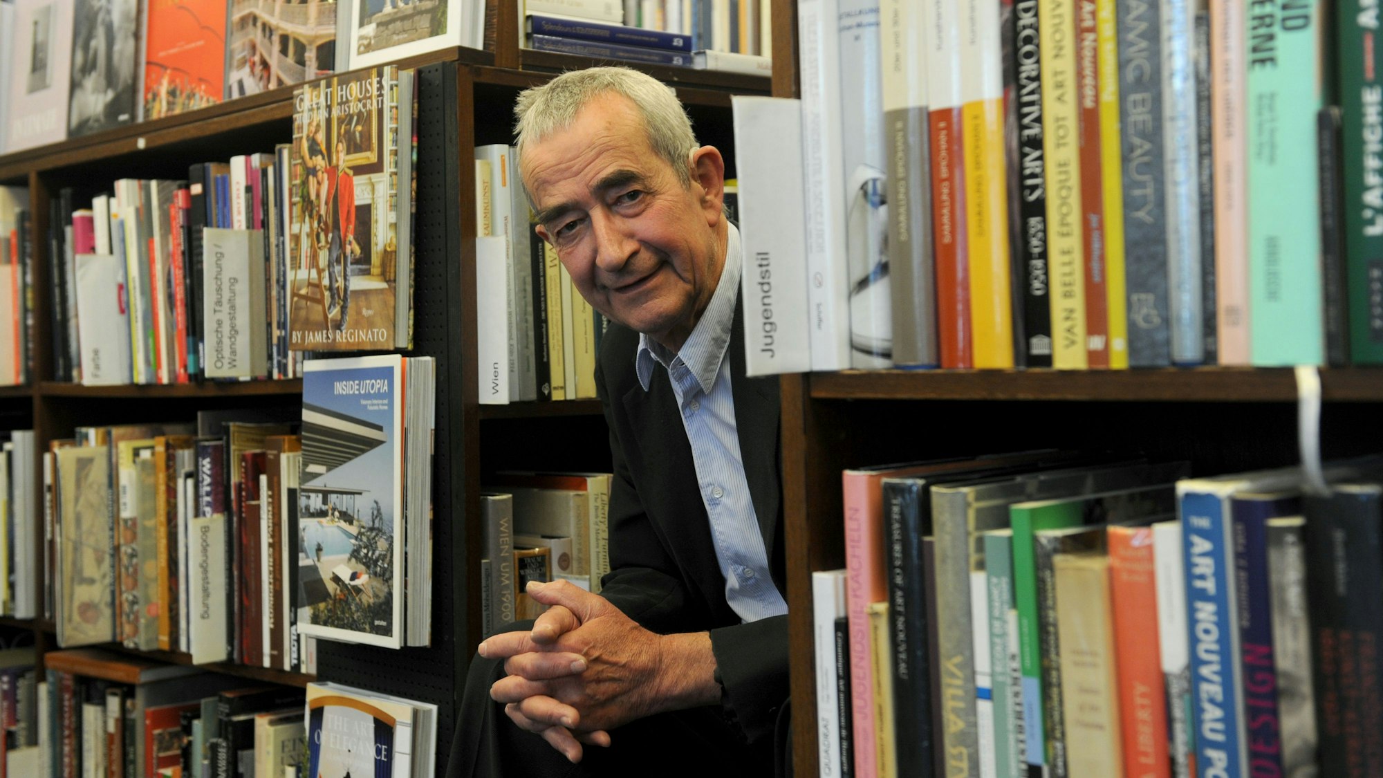 Walther König
schaut zwischen Bücherregalen heraus.