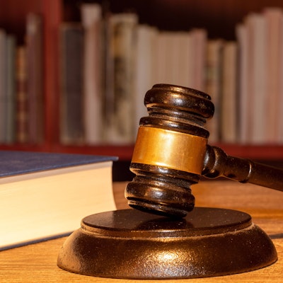 Buch und Richterhammer liegen auf einem Tisch vor einem Bücherregal.