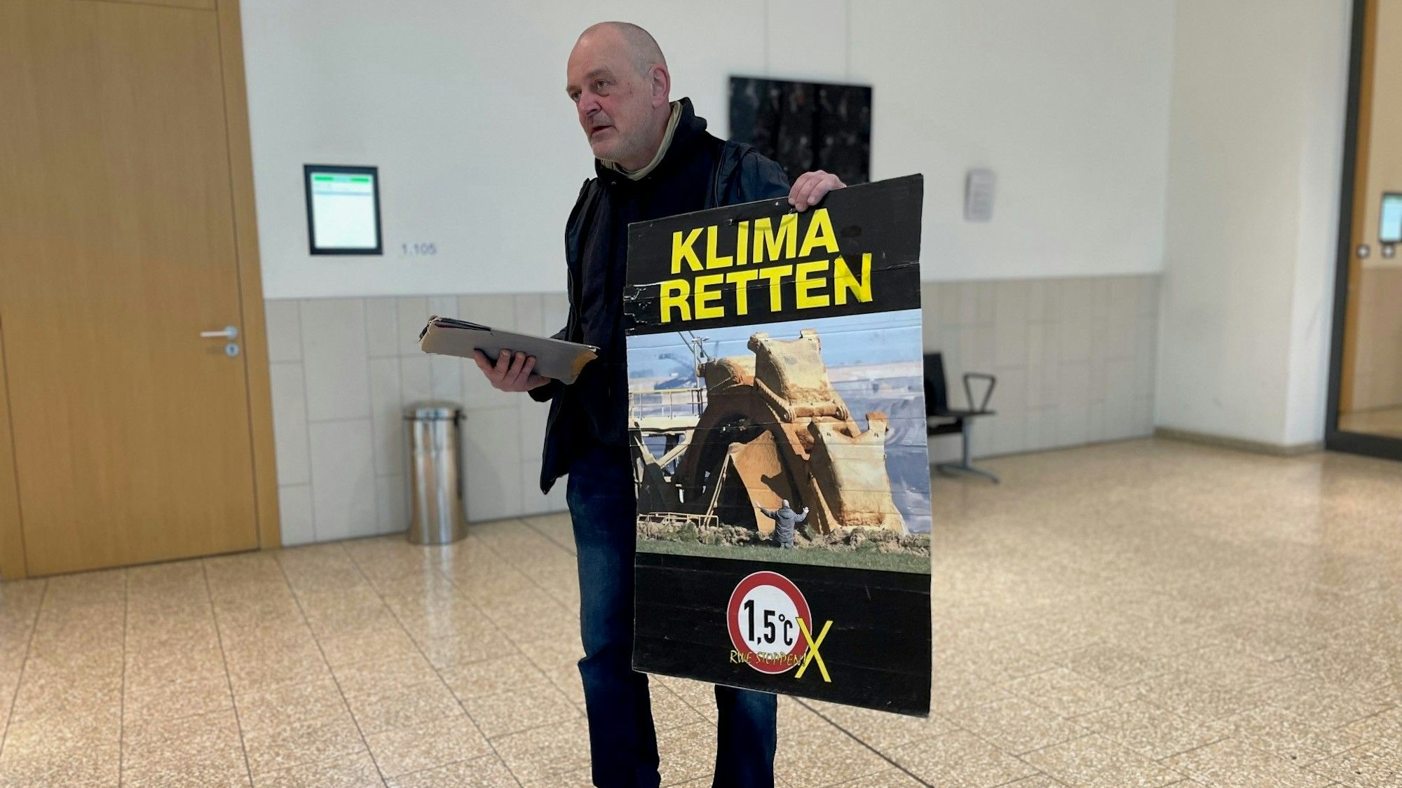 Klima-Aktivist Winfried Bernhard in Düsseldorf vor Gericht. Auf seinem Protestplakat: Das umstrittene Foto, das ihn vor einem Tagebaubagger zeigt. Er steht vor Gericht, weil er ein im Landtag ausgestelltes Bild mit Kartoffelbrei beschmiert hatte. Das als Pressefoto des Jahres ausgezeichnete Bild zeigt ihn selbst, wie er vor einem Braunkohlebagger im Rheinischen Revier kniet.