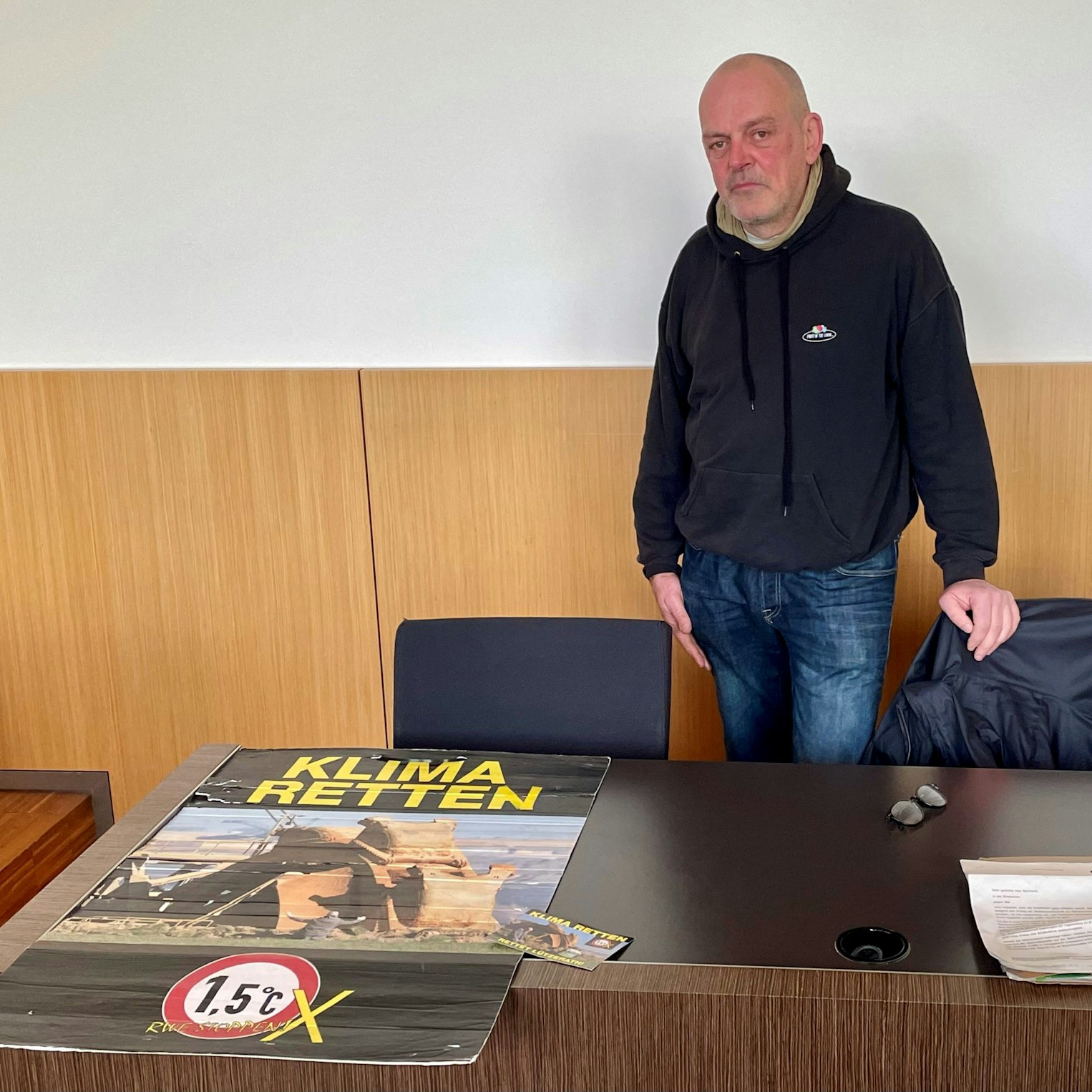 Klima-Aktivist Winfried Bernhard in Düsseldorf vor Gericht. Auf seinem Protestplakat: Das umstrittene Foto, das ihn vor einem Tagebaubagger zeigt. Er steht vor Gericht, weil er ein im Landtag ausgestelltes Bild mit Kartoffelbrei beschmiert hatte. Das als Pressefoto des Jahres ausgezeichnete Bild zeigt ihn selbst, wie er vor einem Braunkohlebagger im Rheinischen Revier kniet.