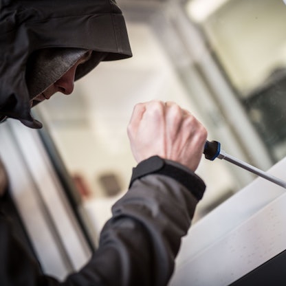 Das Bild zeigt einen Einbrecher, der mit einem Schraubenziehen versucht ein Fenster aufzuhebeln.