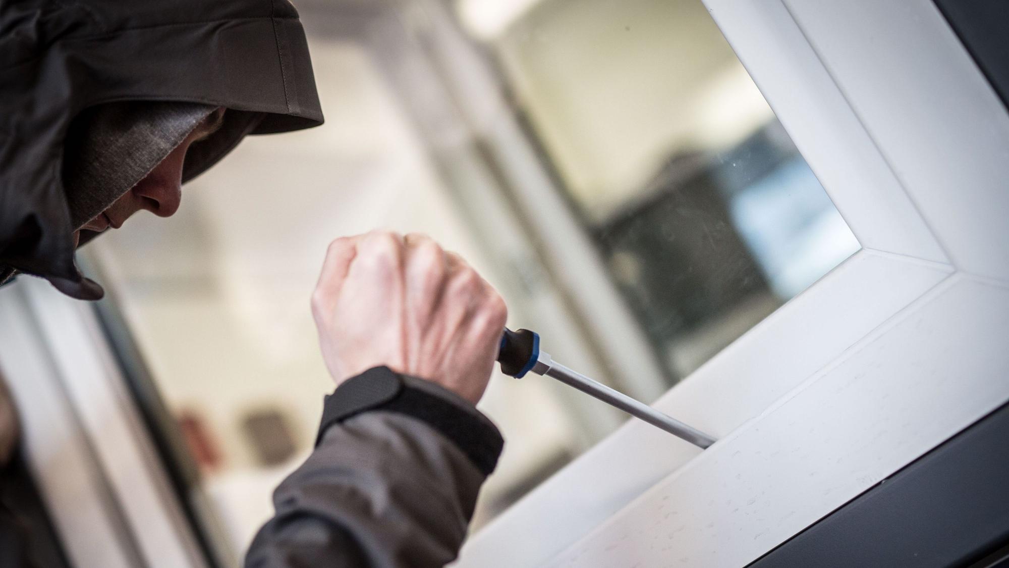 Das Bild zeigt einen Einbrecher, der mit einem Schraubenziehen versucht ein Fenster aufzuhebeln.