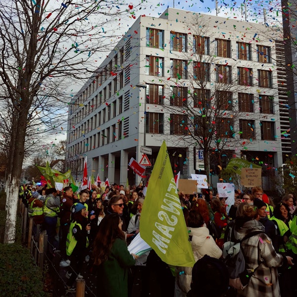 Menschen in grünen Warnwesten und mit Fahnen und Plakaten laufen durch eine Straße