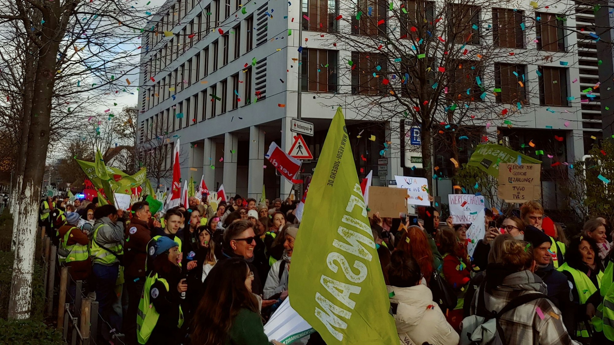 Menschen in grünen Warnwesten und mit Fahnen und Plakaten laufen durch eine Straße