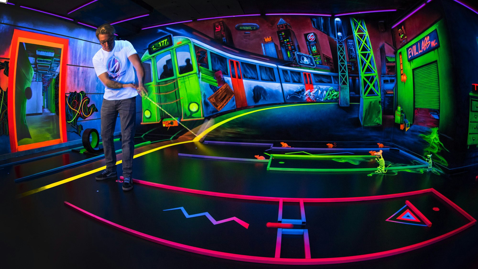 Ein Mann schlägt auf einer Neon-leuchtenden Bahn mit Fantasie-Motiv im Hintergrund ab. Schwarzlicht, also ultraviolettes Licht, lässt alles leuchten.