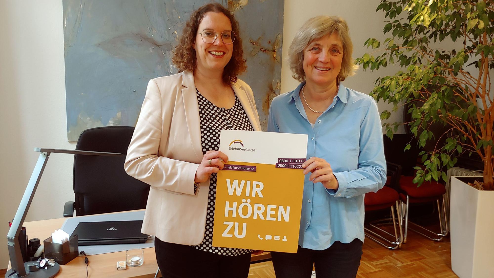 Zwei Frauen, die ein Plakat mit der Aufschrift "Wir hören zu" in die Kamera halten