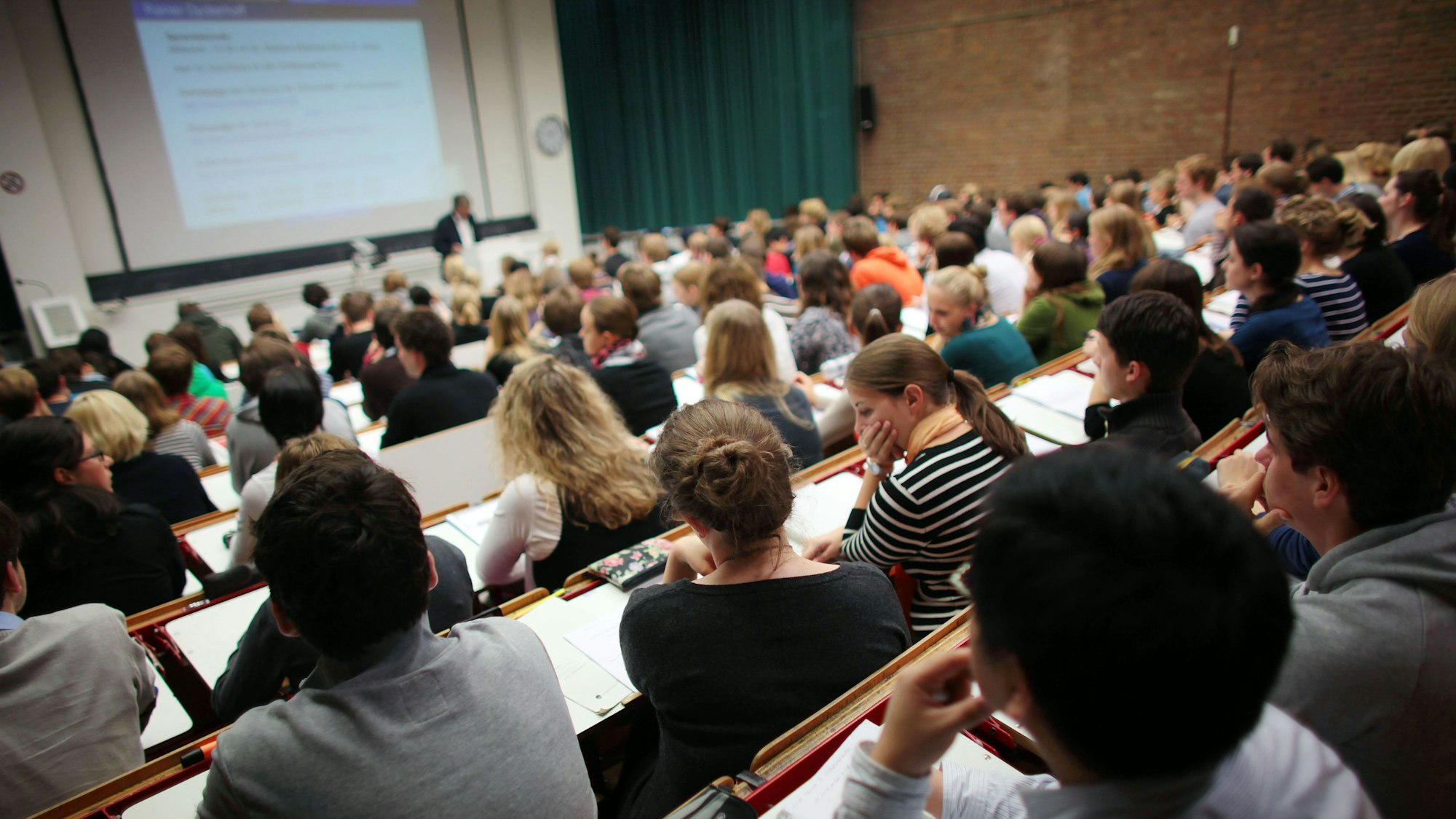 Studierende sitzen in einem Hörsaal der Universität und verfolgen eine Vorlesung.