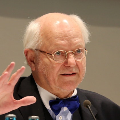 Franz Xaver Ohnesorg spricht in ein Mikro. Er trägt einen dunklen Anzug und eine blaue Fliege.