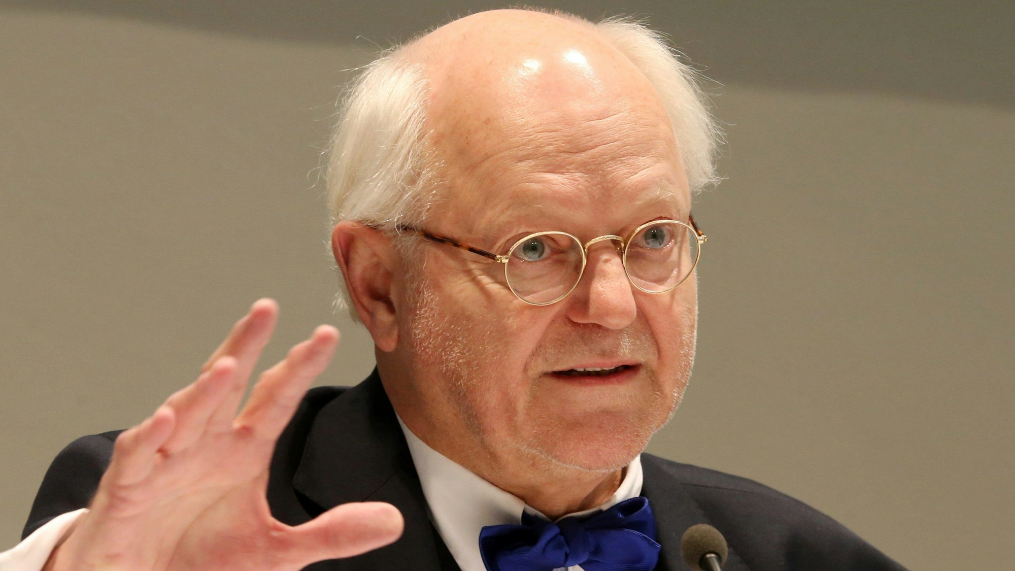 Franz Xaver Ohnesorg spricht in ein Mikro. Er trägt einen dunklen Anzug und eine blaue Fliege.