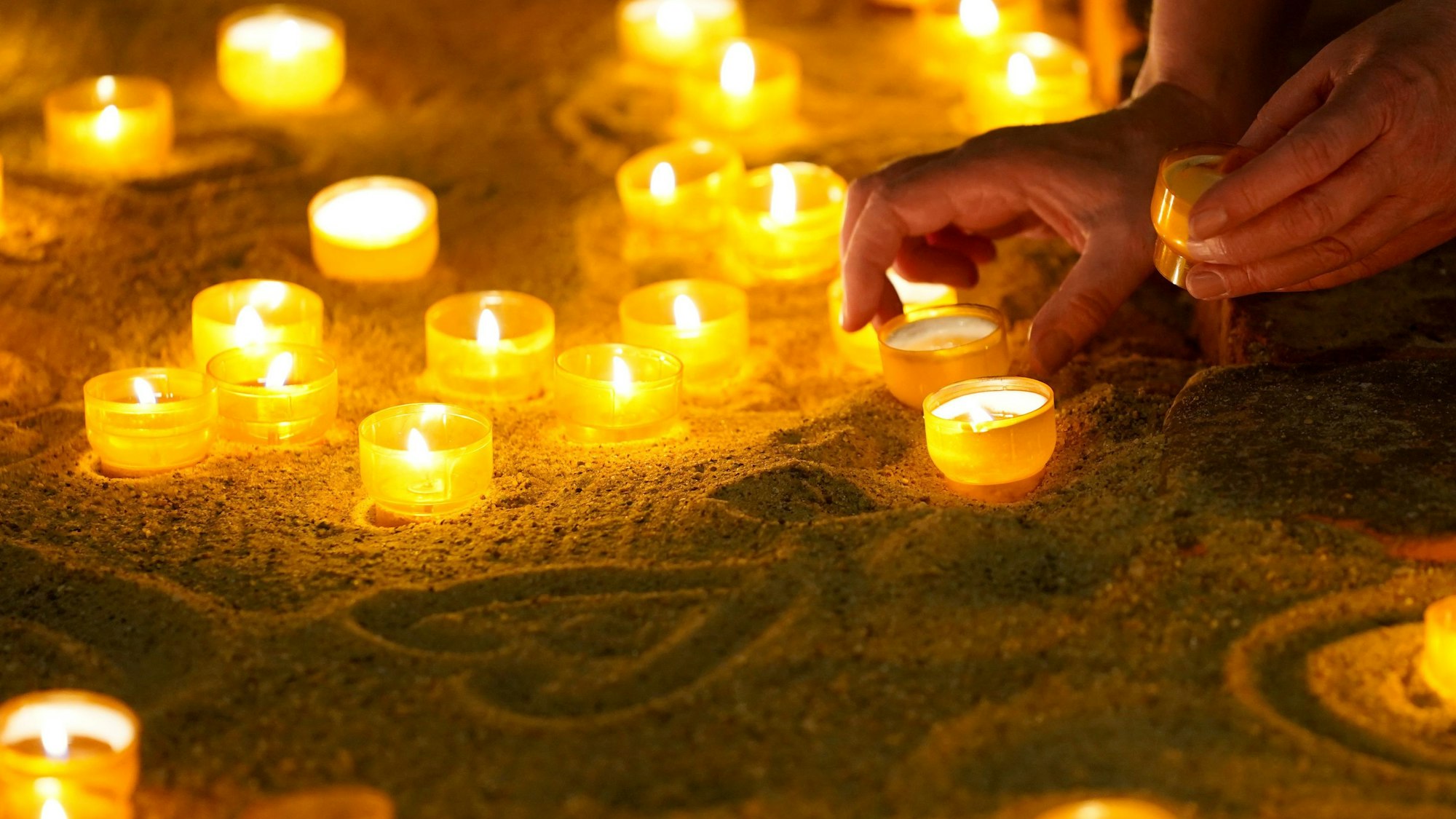 Eine Hand zündet Teelichter zum Gedenken an.