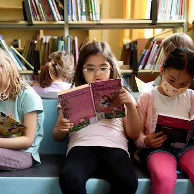 Mädchen sitzen auf einem bunten Podest und lesen in Büchern.