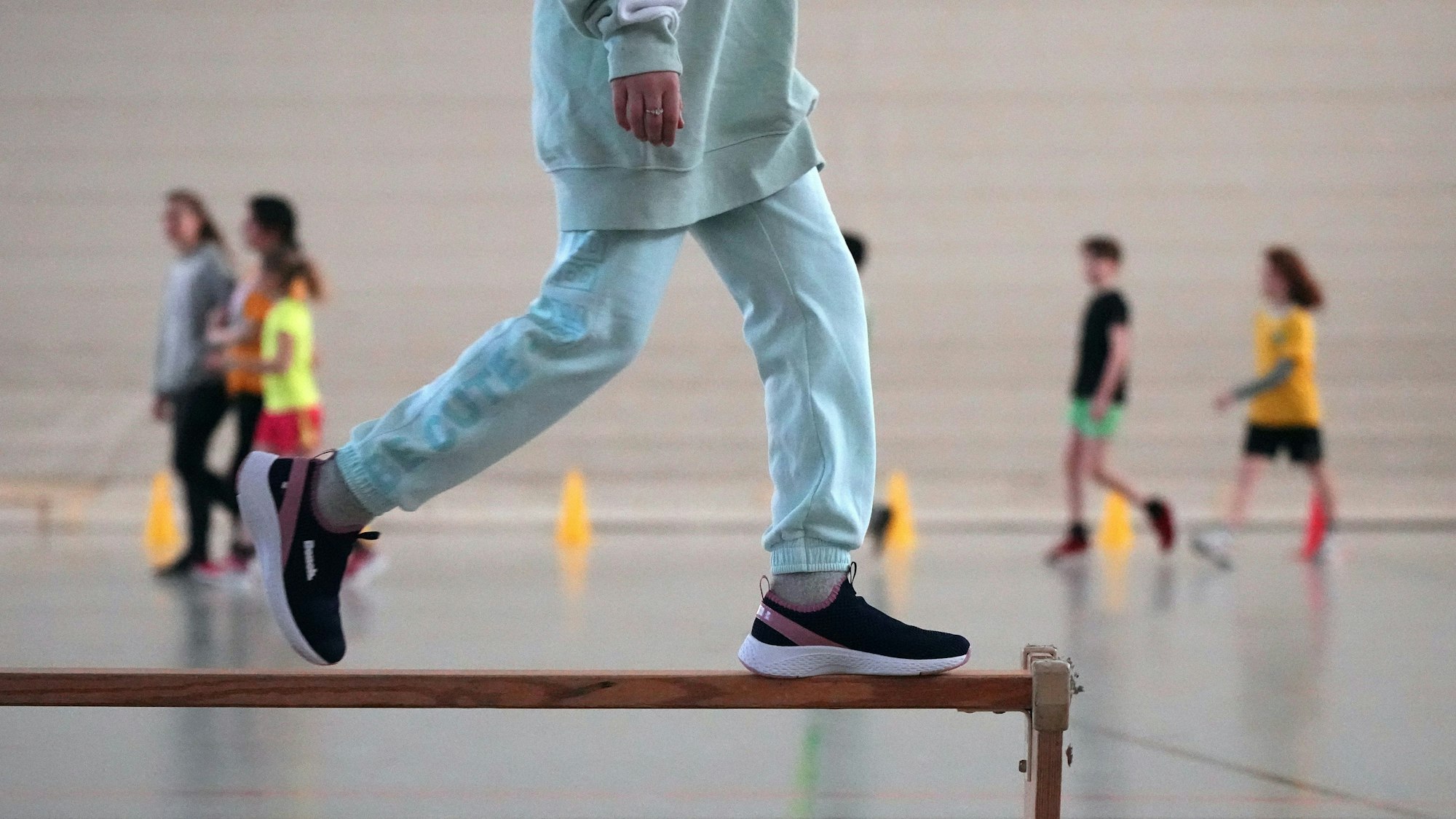 Eine Schülerin läuft im Sportunterricht über eine umgedrehte Holzbank.