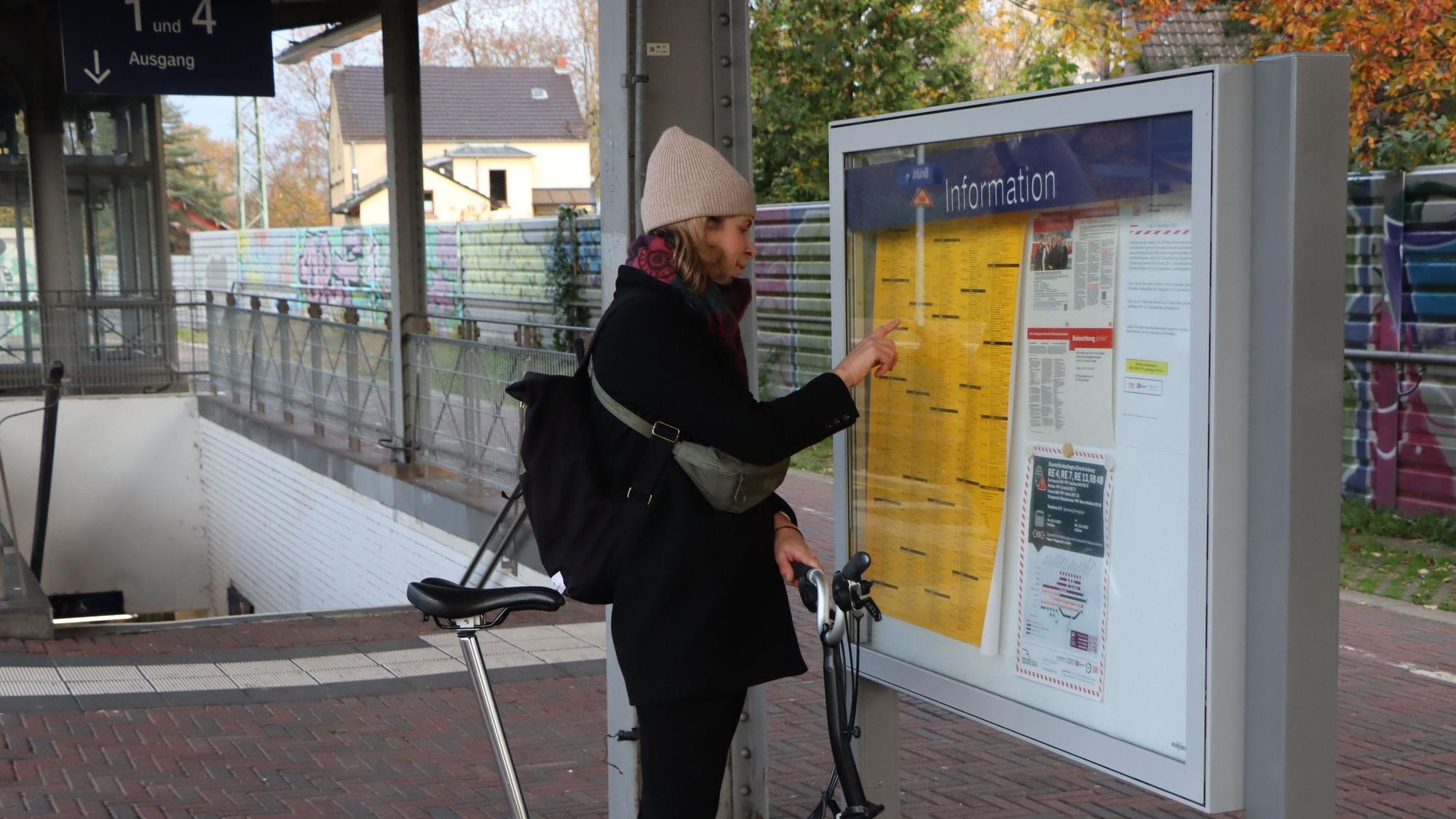 Das Bild zeigt eine Frau auf dem Bahnhof in Brühl vor dem Fahrplan.