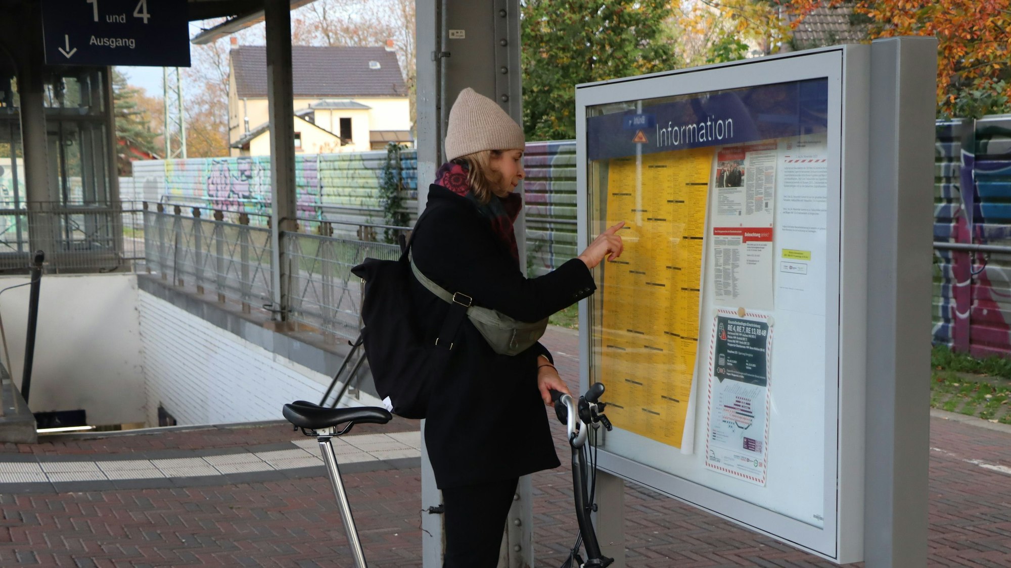 Das Bild zeigt eine Frau auf dem Bahnhof in Brühl vor dem Fahrplan.