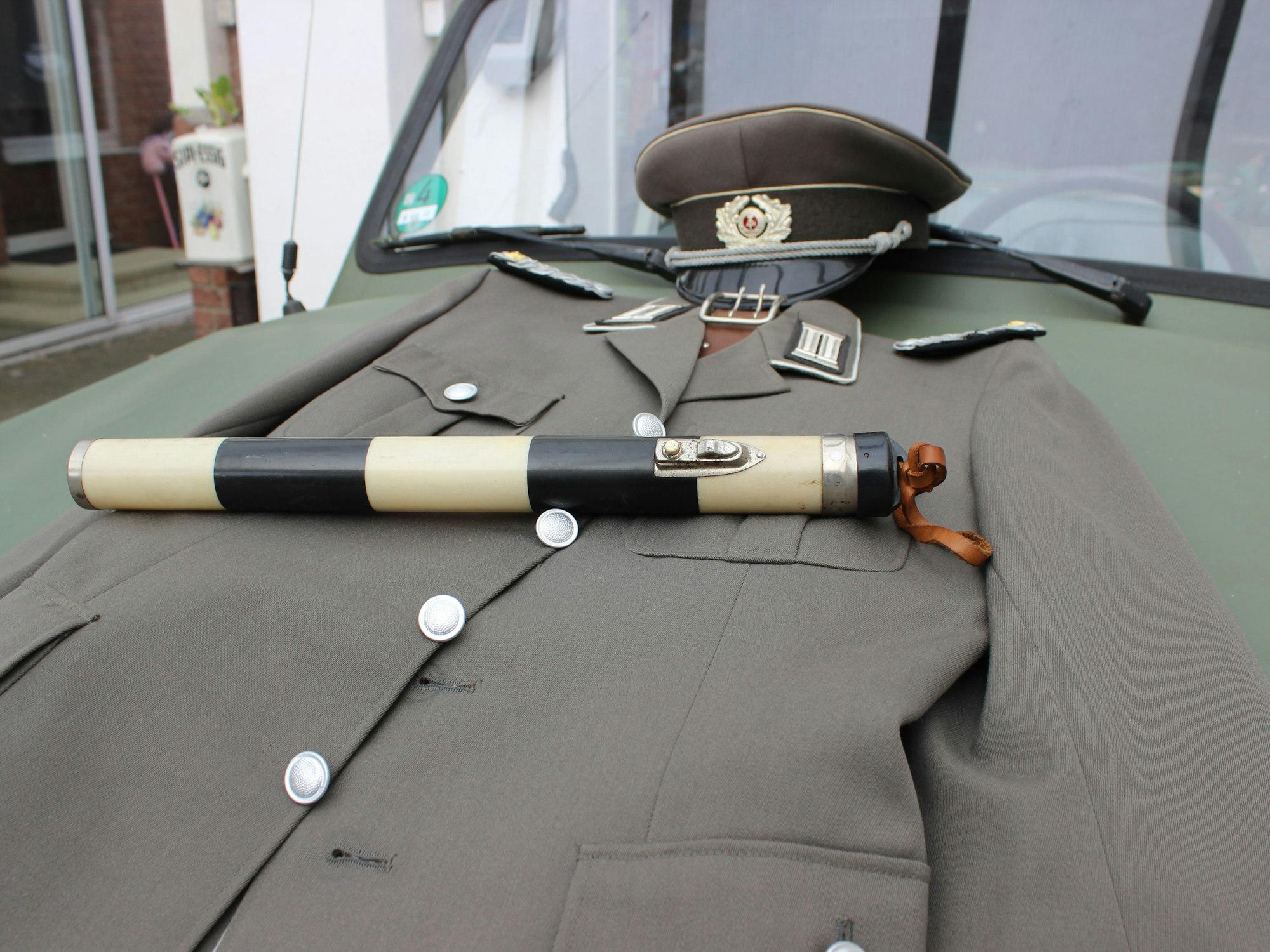 Eine NVA-Uniform und ein Regulierstab liegen auf der Motorhaube.