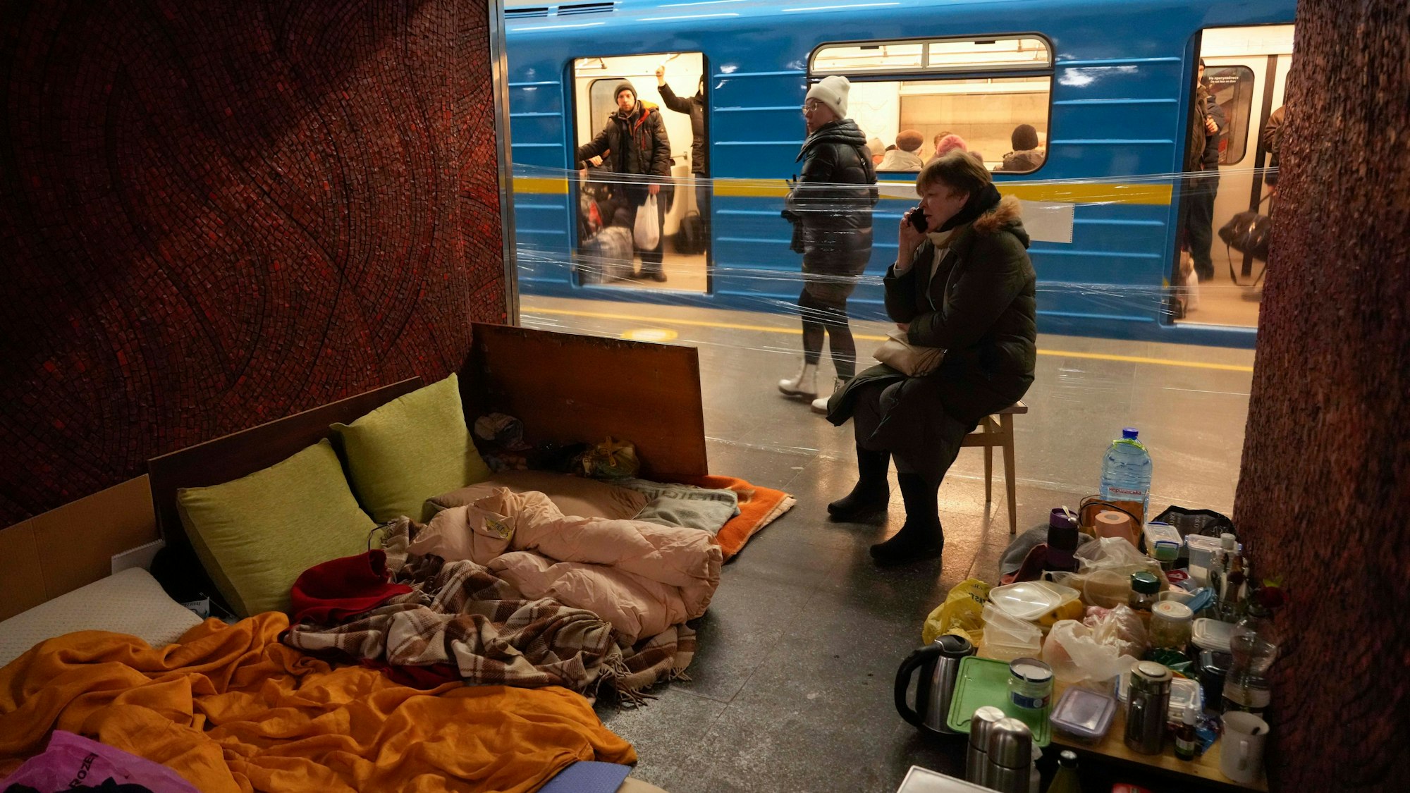 Ein Bild aus dem März 2022: Eine Frau sitzt mit ihren Habseligkeiten und Lebensmitteln auf einem Stuhl in einem improvisierten Schutzraum in einer U-Bahn-Station in Kiew, die von den Bewohnern der Stadt als Bombenschutzraum genutzt wird, während ein Zug vorbeifährt.