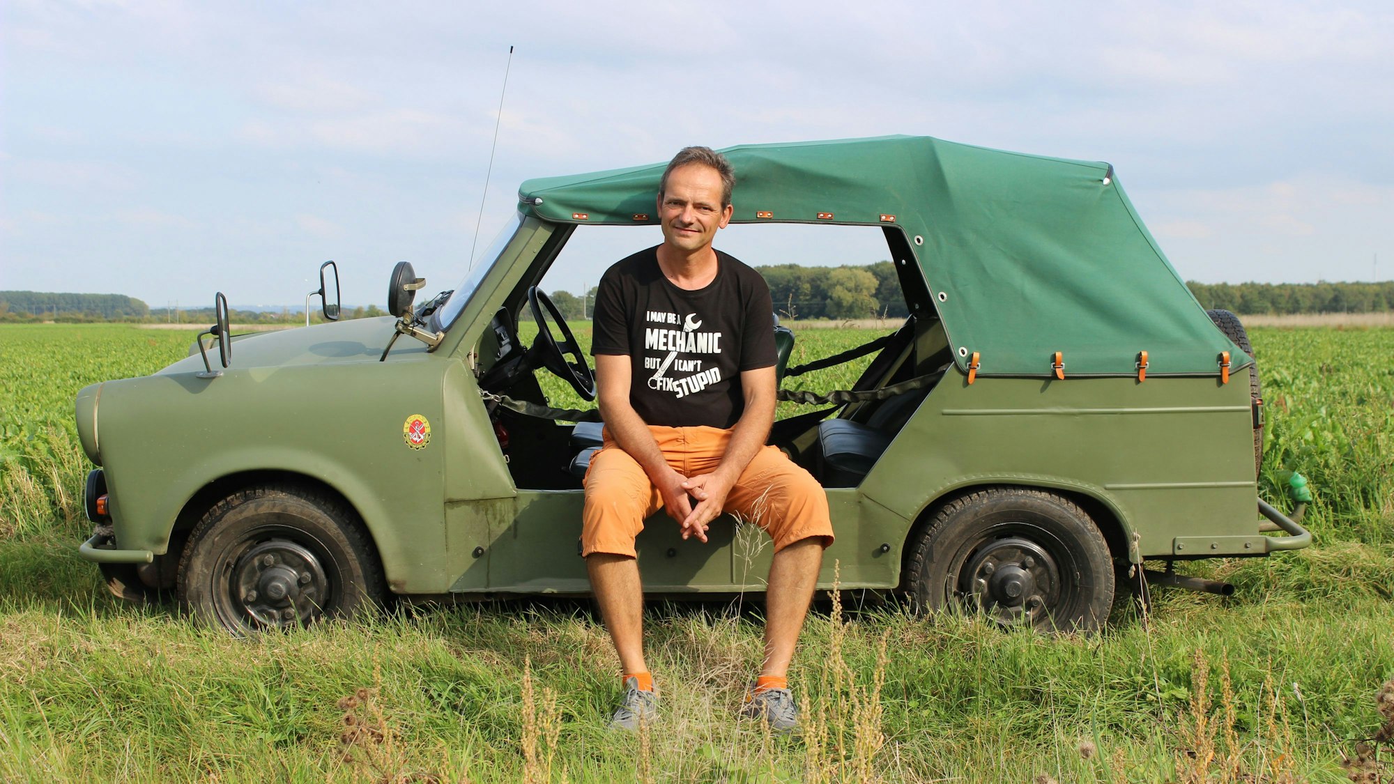 Thilo Gehroldt sitzt auf seinem olivgrünen Trabi, der keine Türen, sondern nur Ketten an den Seiten hat.