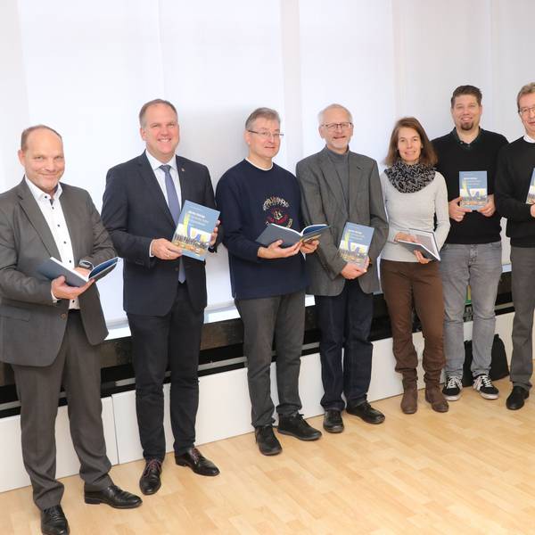 Männer und Frauen halten ein Buch in den Händen.