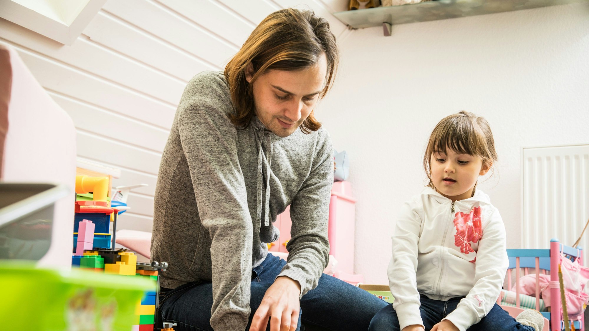 Ein Mann spielt mit Klötzen mit einem Mädchen in einem Kinderzimmer.