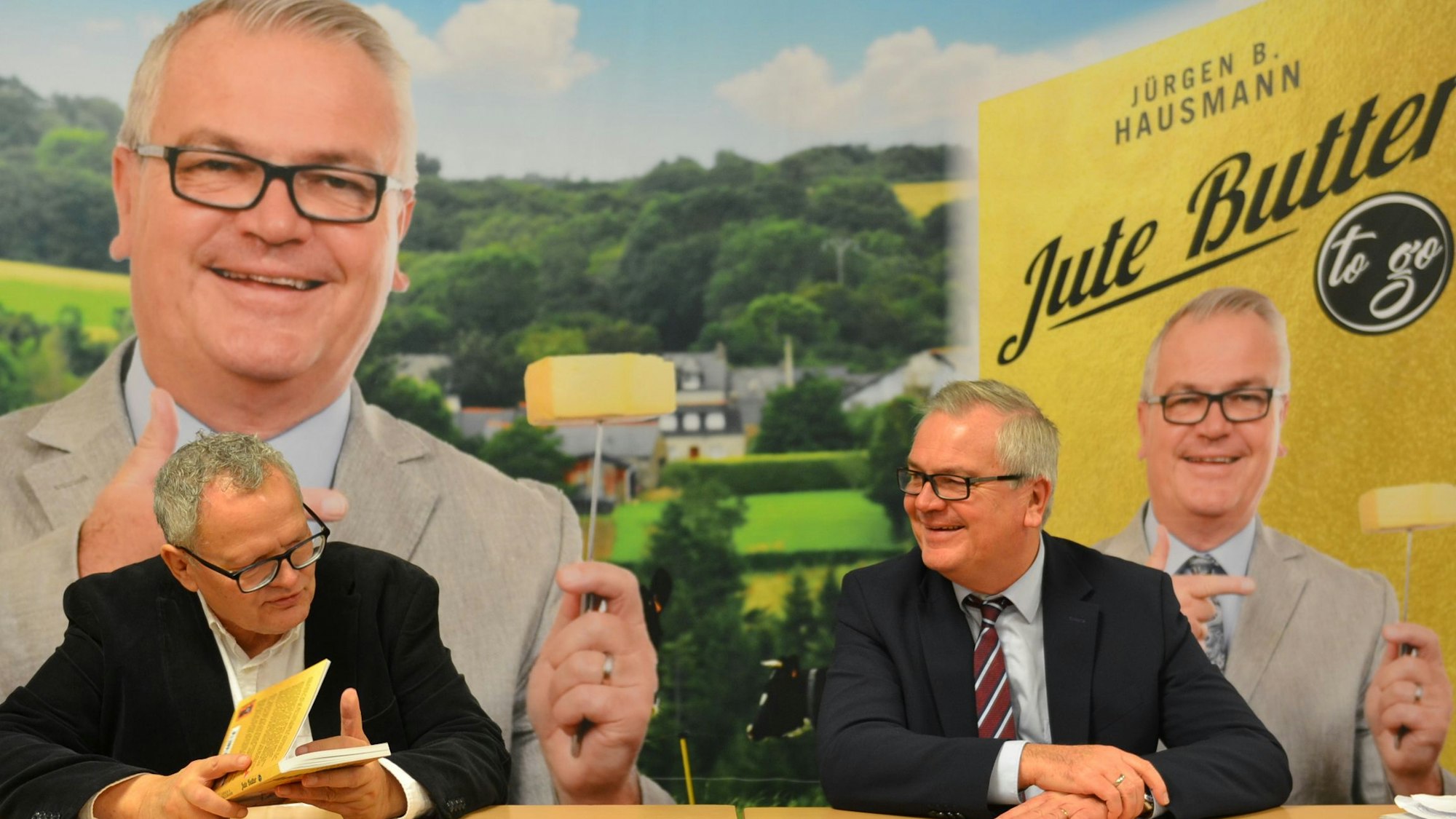 Ulli Potofski und Jürgen Beckers alias Jürgen B. Hausmann sitzen an einem Tisch. Potofski hält Beckers' neues Buch in der Hand.