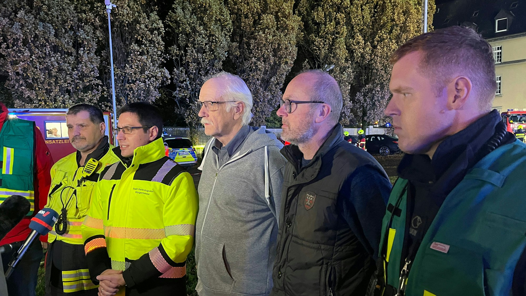 Mehrere Männer stehen aufgereiht vor einem Mikrofon.