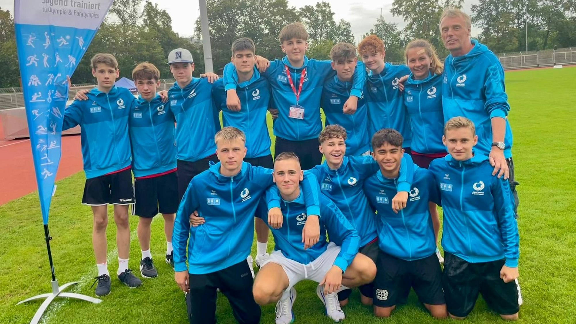 Zu sehen sind das Team und seine Lehrer, gekleidet in blaue Trainingskleidung.