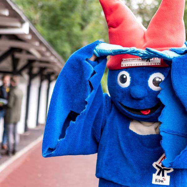Das Maskottchen vom Kinderschutzbund Köln ist ein laues Männchen mit einem roten Hut, der aussieht wie die Spitzen des Kölner Doms.