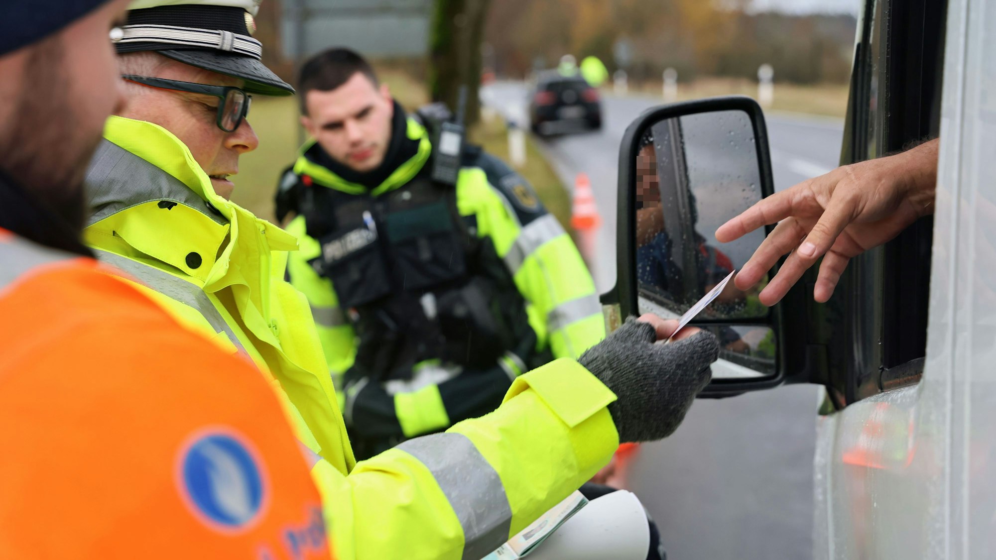 Ein Fahrer reicht seine Papiere aus dem Fenster. Jeweils ein Polizist aus Deutschland, den Niederlanden und Belgien stehen bereit.