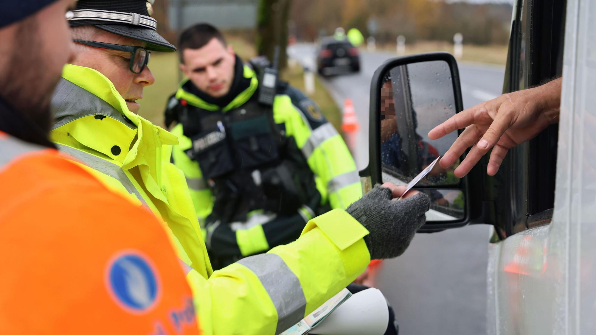 Polizisten kontrollieren am Straßenrand einen PKW durch dessen Fenster hindurch.