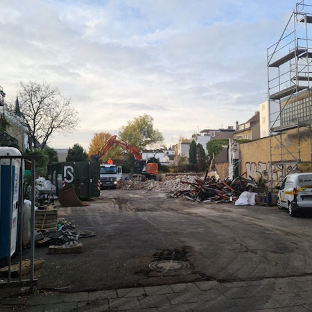 Blick auf ein großes Grundstück, auf dem Trümmer per Bagger auf einen Lastwagen geschaufelt werden.