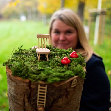 Im Vordergrund befindet sich eine Miniaturlandschaft mit Fliegenpilzen und einem Stuhl, dahinter ist leicht unscharf Julia Mostert zu sehen.