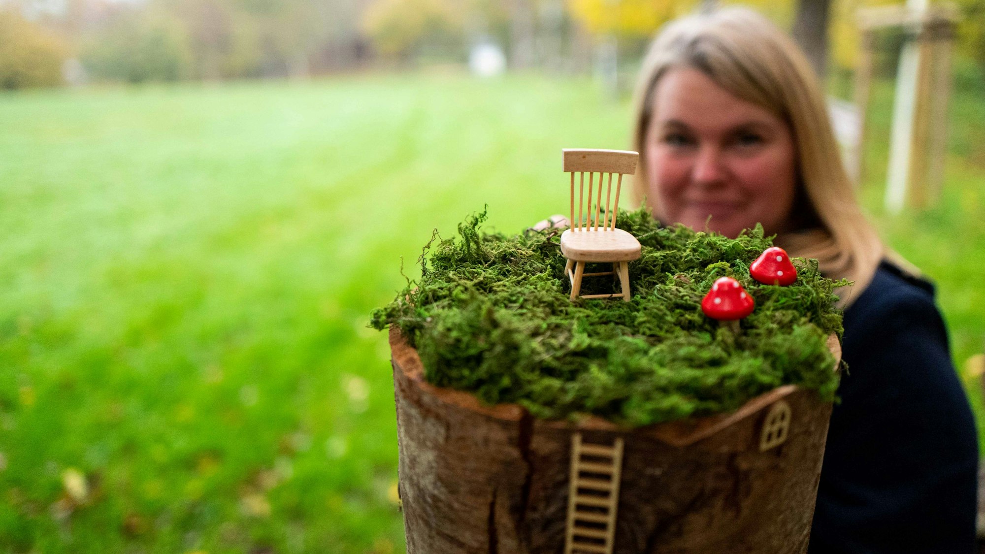 Im Vordergrund befindet sich eine Miniaturlandschaft mit Fliegenpilzen und einem Stuhl, dahinter ist leicht unscharf Julia Mostert zu sehen.