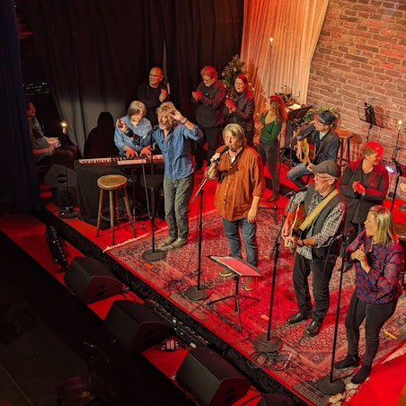 Menschen stehen auf einer Bühne, die einem Wohnzimmer nachempfunden ist.