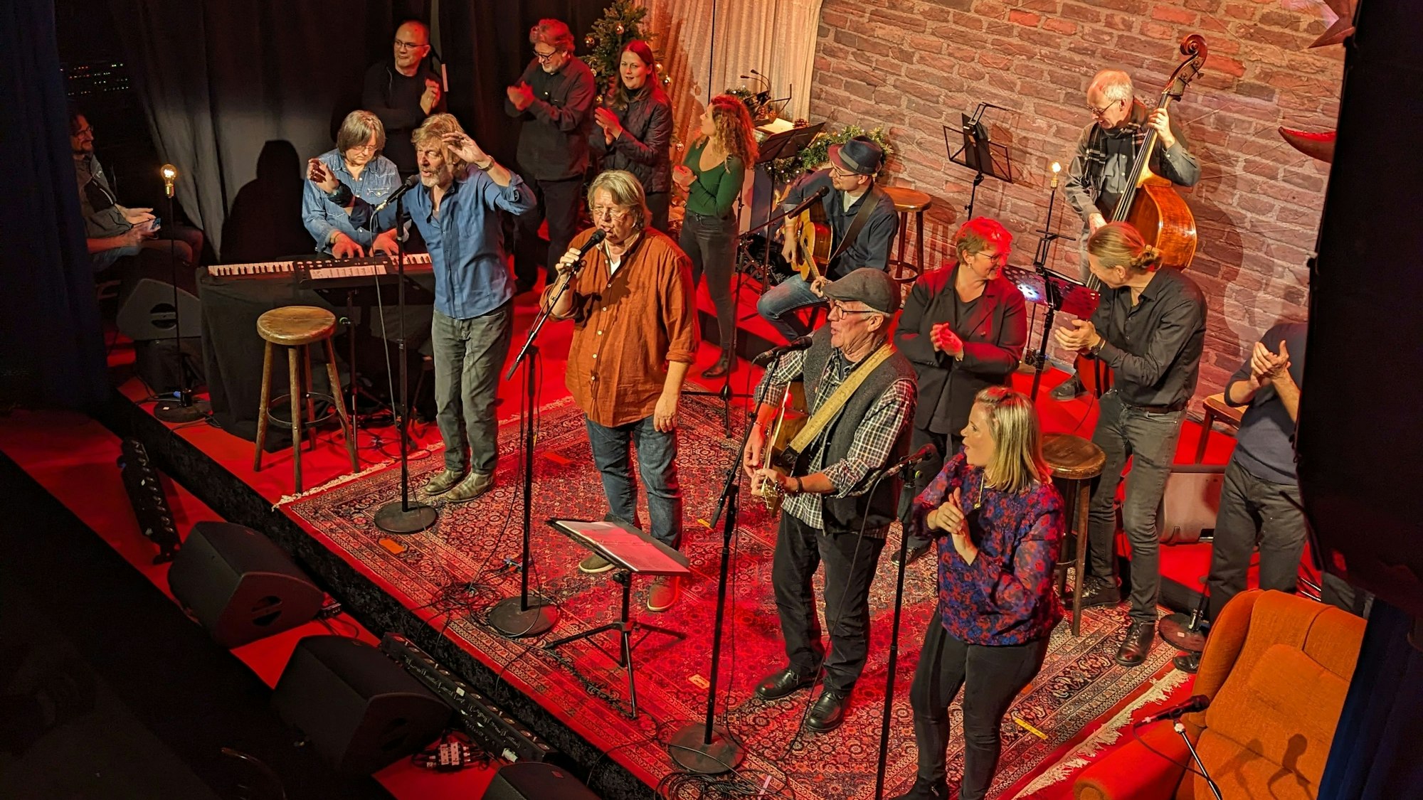 Menschen stehen auf einer Bühne, die einem Wohnzimmer nachempfunden ist.