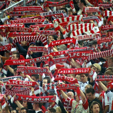 Anhänger des 1. FC Köln halten ihre Fan-Schals in die Höhe.