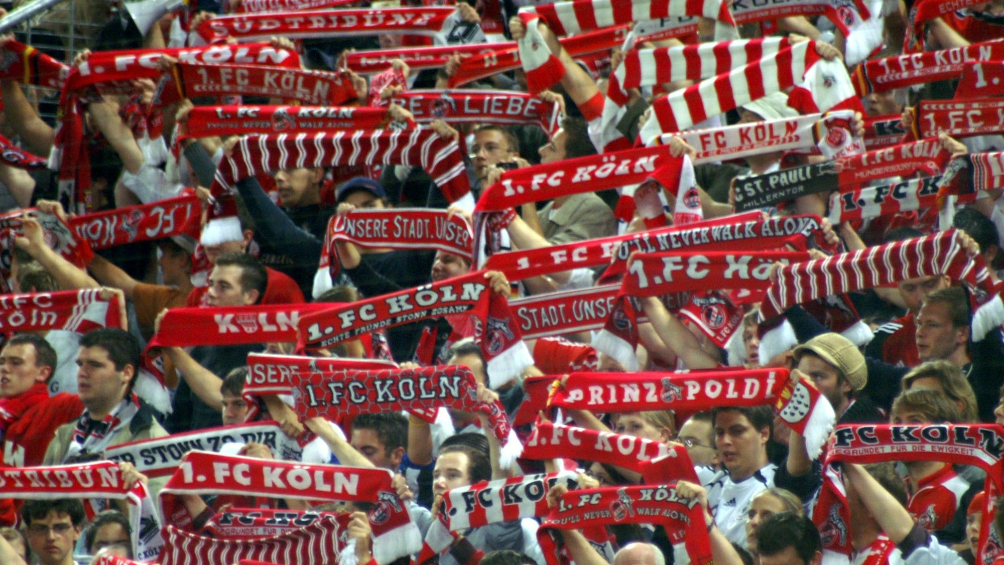 Anhänger des 1. FC Köln halten ihre Fan-Schals in die Höhe.