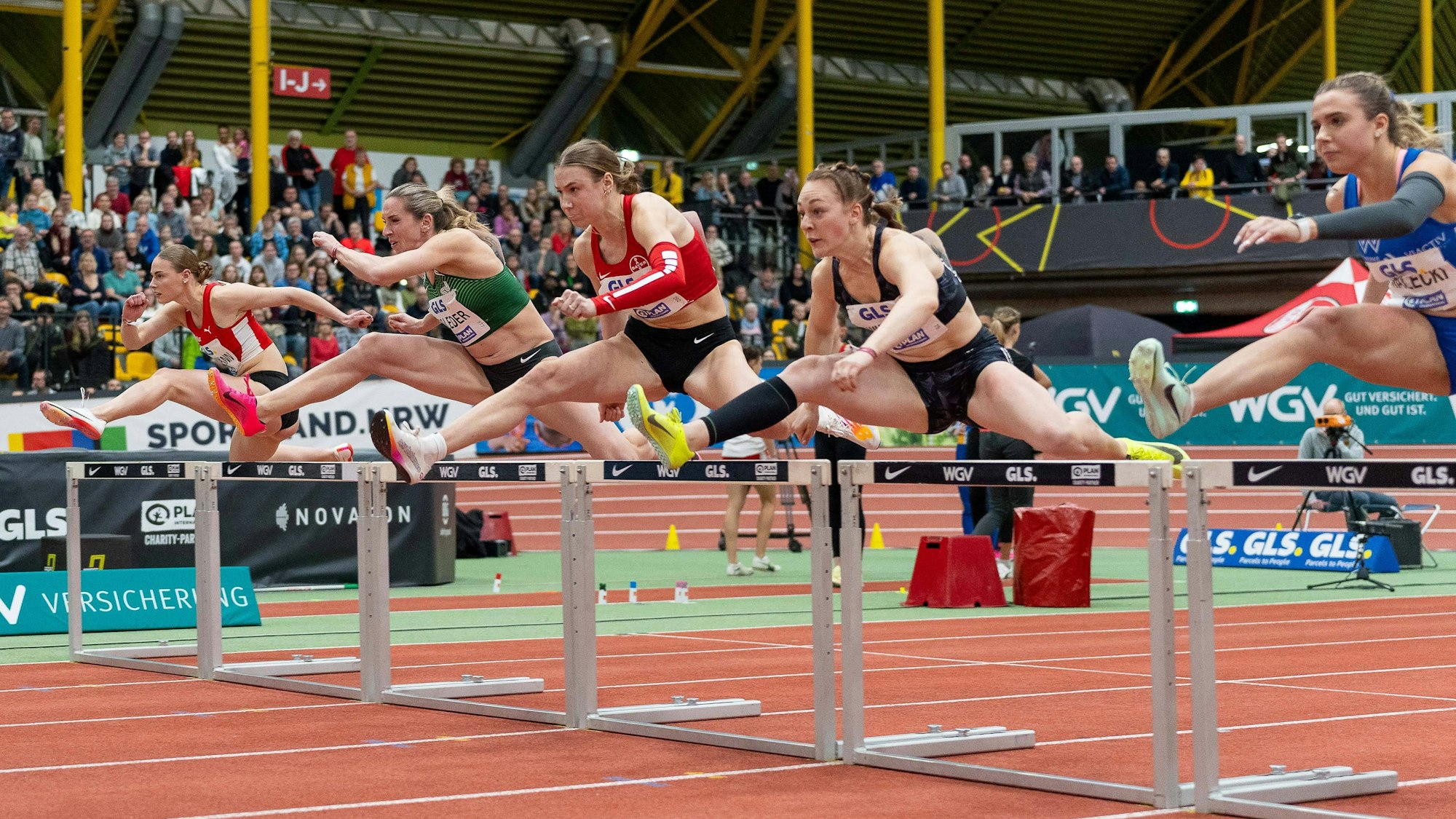 Das Bild zeigt fünf Sportlerinnen beim Hürdenlauf.