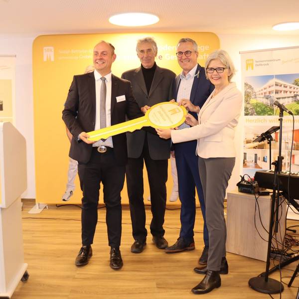 Drei Männer und eine Frau halten gemeinsam einen überdimensionalen Schlüssel.