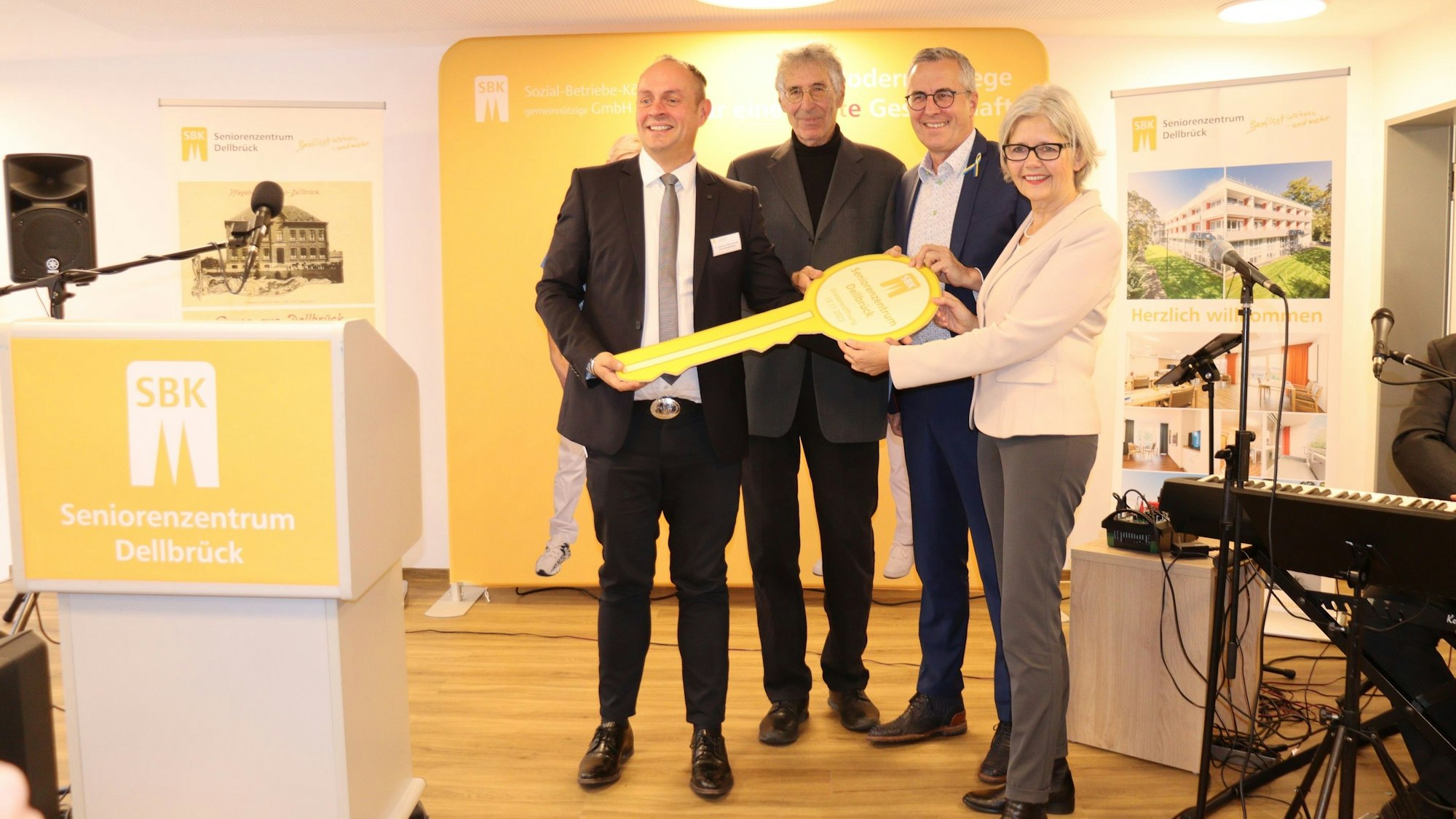 Drei Männer und eine Frau halten gemeinsam einen überdimensionalen Schlüssel.