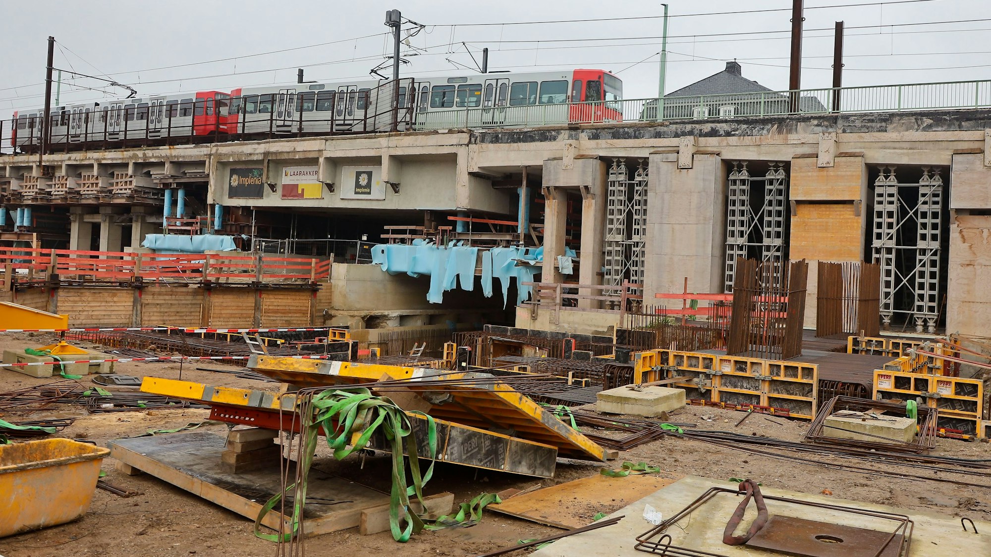 Blick auf Betonfundamente, im Hintergrund sind eine Stadtbahn auf der Brückenrampe sowie Betonteile zu sehen.