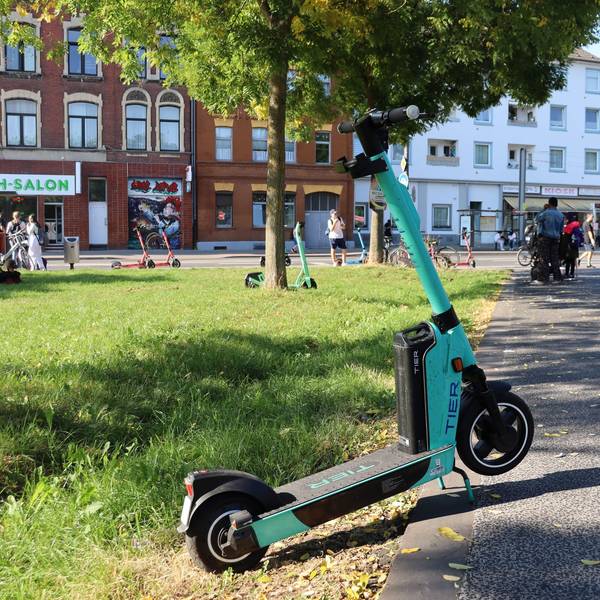 Ein E-Scooter steht halb auf einem Weg und halb auf einer Rasenfläche daneben.
