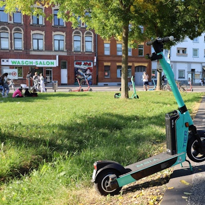 Ein E-Scooter steht halb auf einem Weg und halb auf einer Rasenfläche daneben.