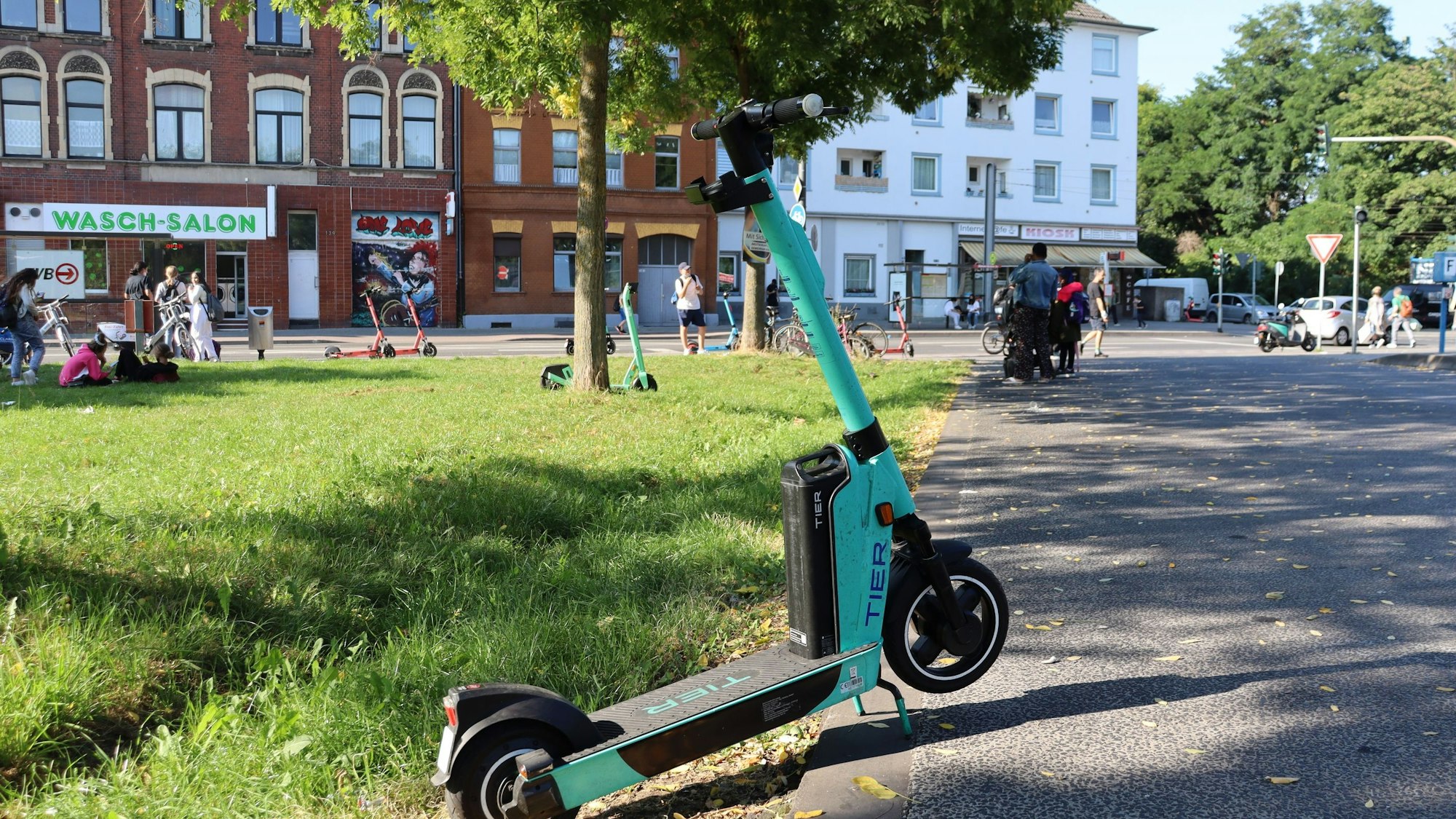 Ein E-Scooter steht halb auf einem Weg und halb auf einer Rasenfläche daneben.