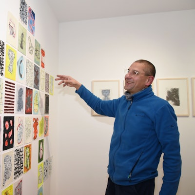 Ein Mann steht vor einer Wand mit vielen in Reihen angeordneten kleinformatigen Zeichnungen.