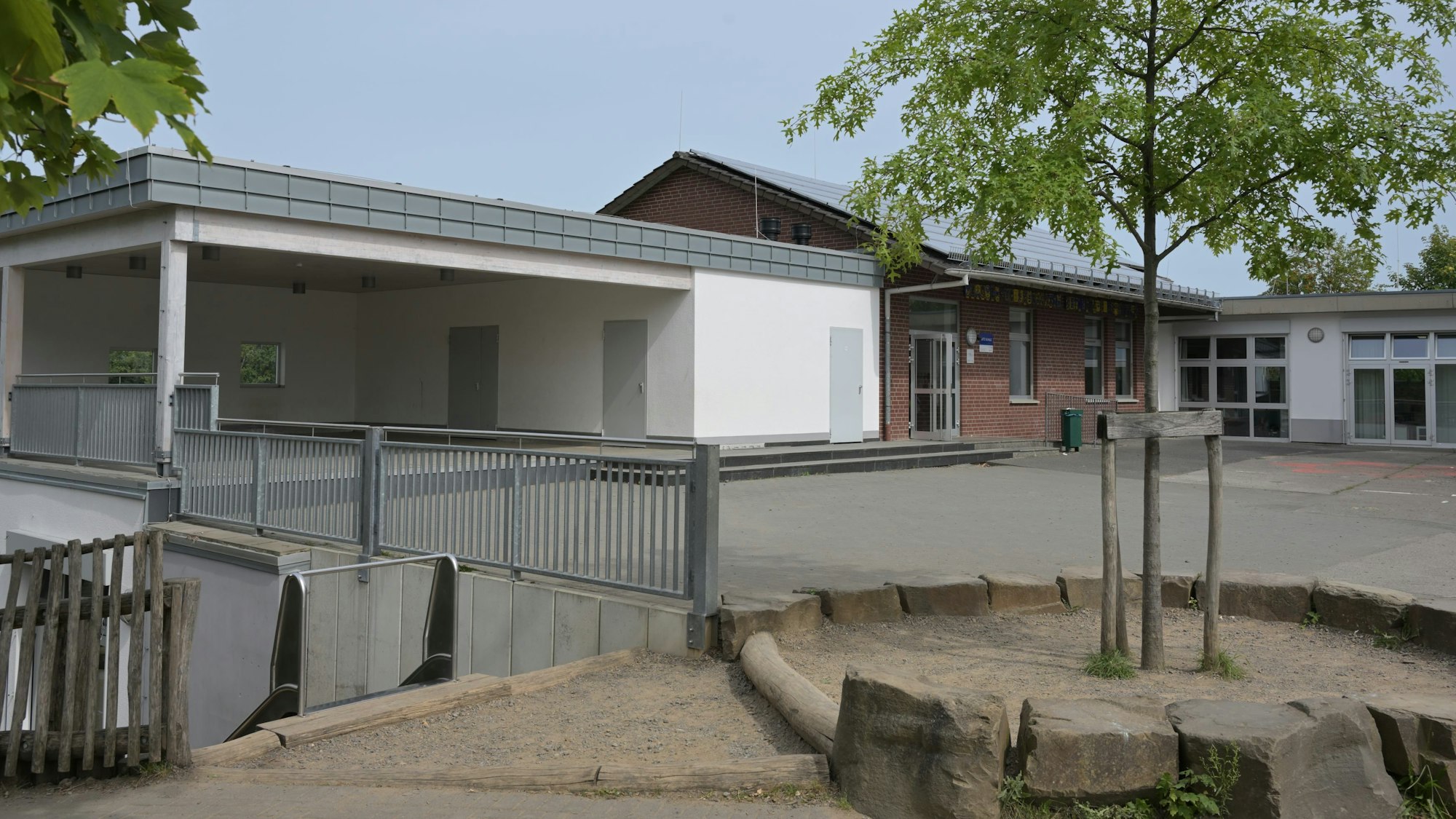 Der L-förmige Bau der KGS Burg Berge in Blecher formiert sich um den Pausenhof. Im Vordergrund ein Spielgelände mit einem jungen Laubbaum.