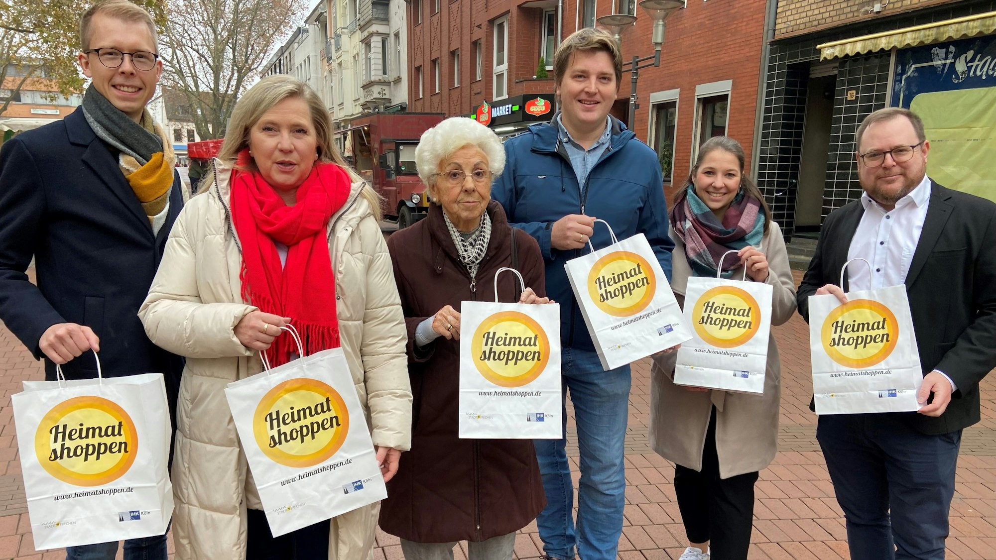 Auf dem Bild sind fünf Menschen zu sehen, die eine besondere Einkaufstüte präsentieren.