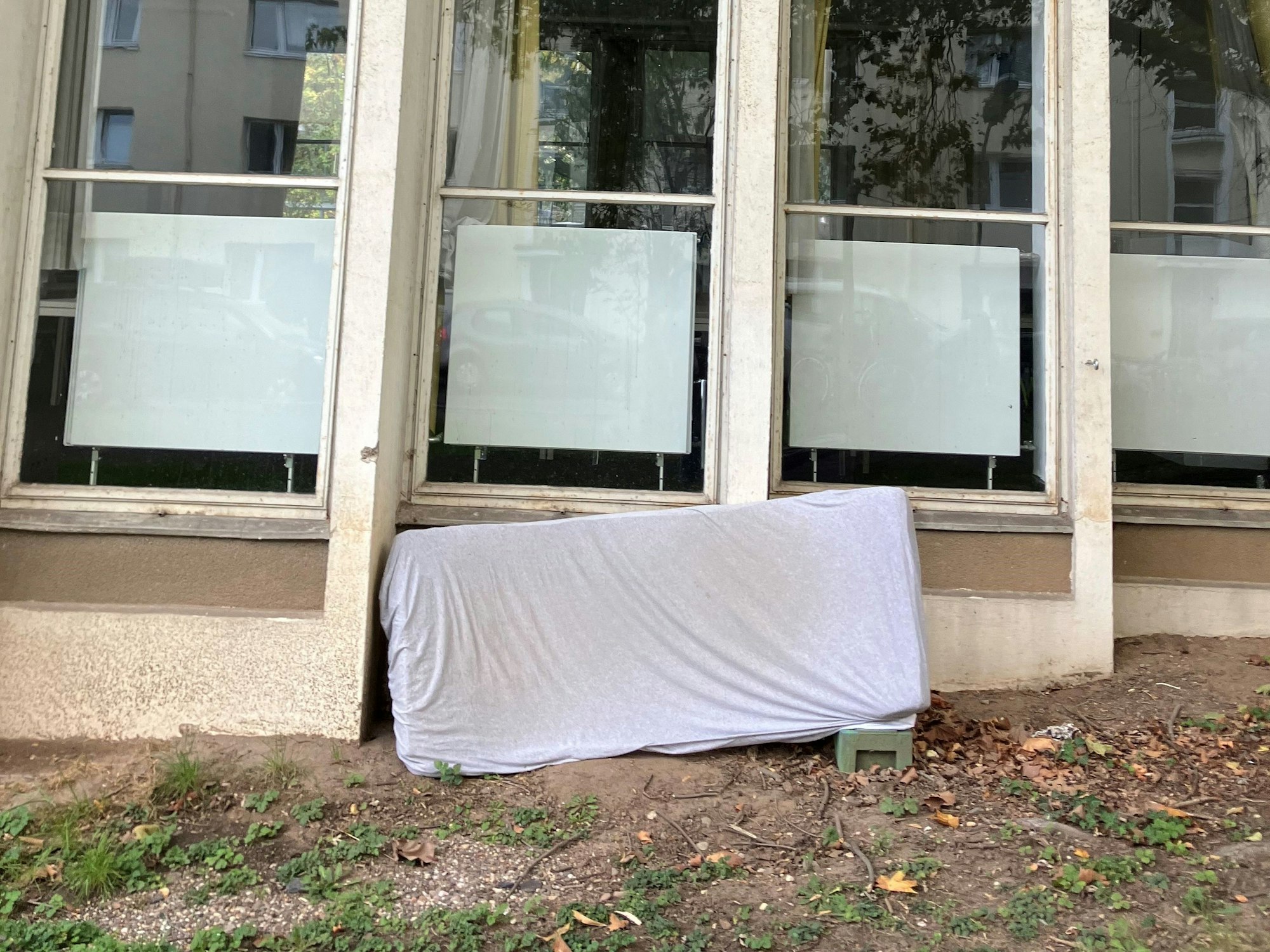 Eine alte Matratze lehnt an einem Gebäude mit großen Fenstern.